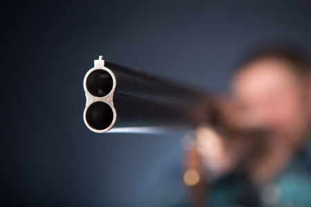 Gangster aiming with a shotgun. Grey backdrop portraitの写真素材
