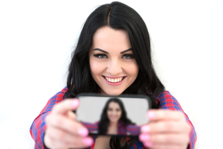 Girl in a plaid shirt makes selfie. Portrait of a smiling cute woman making selfie photo on smartphone isolated on a white backgroundの写真素材