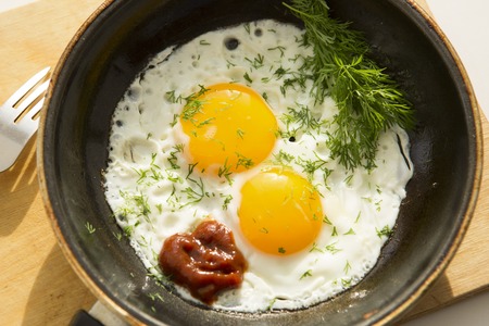 Fried eggs in pan with handle on wooden tableの写真素材