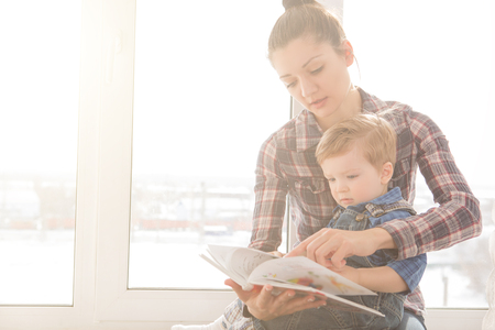 Mother reading with her son on a background of the window in the house. The concept of happiness and love.の写真素材
