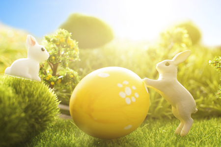 Rabbits with easter eggs on green meadow over sundown. Cute Little easter bunny on spring flowers and green grass. Sunbeams.の写真素材