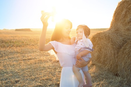 Mother and her child playing with the toy airplane in spring field over soft sunlightの写真素材