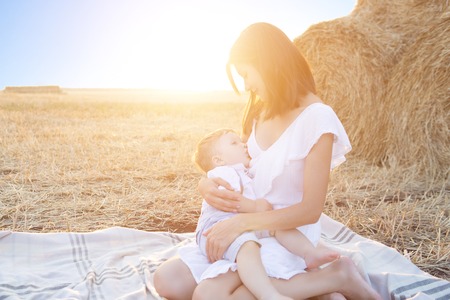 Beautiful baby beeing breastfed in summer field over a sunset.の写真素材