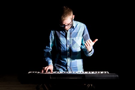 Young musician in plaid shirt playing electric piano in a nightclub over dark background.の写真素材