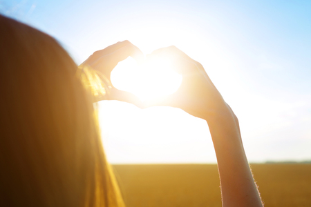 Girl making heart symbol with her hands at sunset on nature background.の写真素材