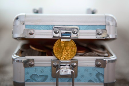 Box for savings full of coins with one dollar coin on wooden table.の写真素材