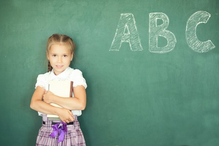 Portrait of caucasian happy child girl with books. School chalkboard or blackboard background. Free text copy space. Education and school concept.の写真素材