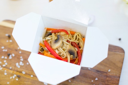 Noodles with pork and vegetables in take-out box on wooden tableの写真素材