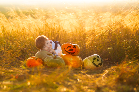 Cute boy enjoying autumn time. Little boy with pumpkins for Halloween over sunset or sunrise background.の写真素材
