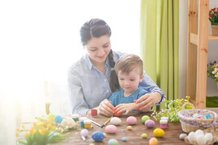 Happy family mother and child boy paints eggs for Easter at home. Family celebrating Easter.