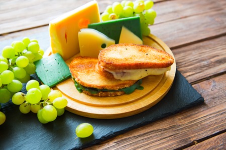 Two hot grilled or fried sandwich with cheese and green grapes on black slate cheeseboard on wooden table.の写真素材
