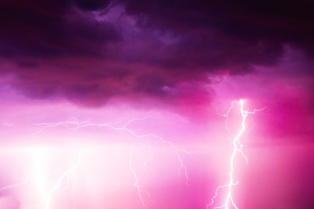 A lightning strike on the cloudy sky. Pink, lilac and purple toned image.の写真素材