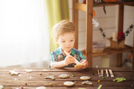 Happy Halloween. Beautiful happy little preschool kid boy covering cookies for Halloween cookies at home. Child celebrating traditional festival halloween or thanksgiving.の写真素材