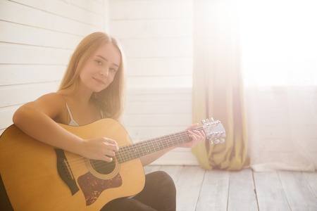Beautiful young woman sitting on the floor in casual clothes at home and playing guitar.の写真素材