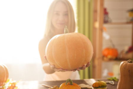 Ready to halloween invasion. Smiling young woman showing big orange pumpkin in halloween decorated kitchen.の写真素材