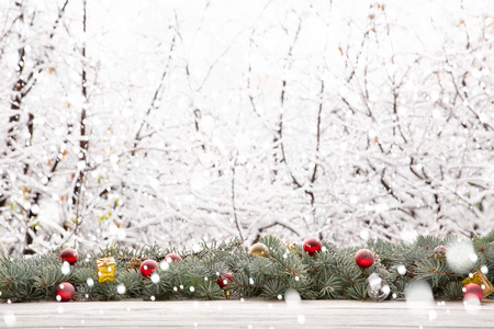 Garland of pine or fir tree branches and Christmas decorations against the background of falling snow and snow-covered forest. Fairy taleの写真素材