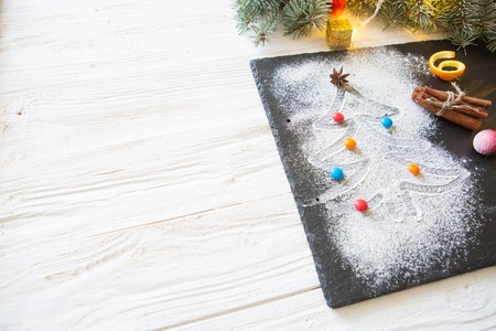 White Christmas tree made of flour, decorated colorful candies with anise star, dry orange peel and cinnamon stick on black slate surface.の写真素材