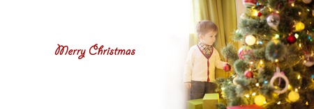 Cute little boy decorating Christmas tree with white space for textの写真素材