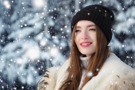 Cute young woman playing with snow in fur coat outdoors.の写真素材