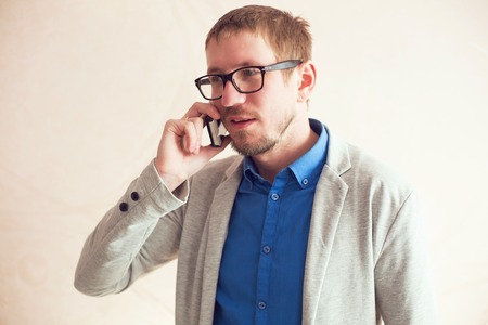 Portrait of a handsome man standing near window and talking on the phoneの写真素材