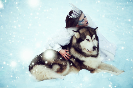 Snow-queen. Fairy tale girl with Huskies or Malamute. Beautiful snow queen witn dogs. Christmas.の写真素材