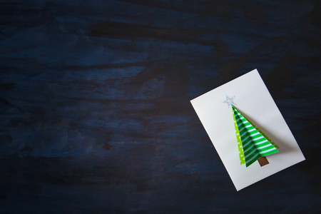 Homemade christmas postcard on dark black background. Green christmas tree on white on postcard.の写真素材