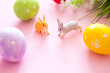 Composition with Easter eggs with rabbits or hare toys and flowers on a pink wooden background.