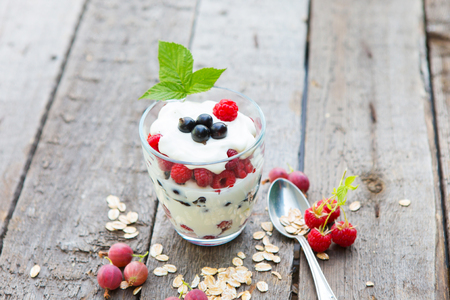 Sweet dessert in glass with berry fruit and whipped cream on a wooden table.の写真素材