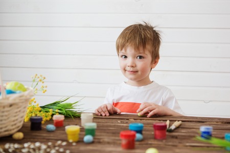painted and decorated eggs for Easter. Portrait of a cute boy 3 years old. He holds a brush and paints Easter eggsの写真素材