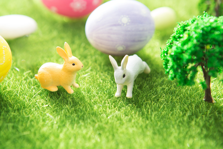 Two rabbit toys with easter eggs on a meadow grass. Yellow easter egg spring meadow with a two rabbit and easter eggs. Fairy taleの写真素材
