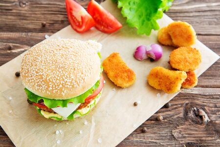 Delicious fast food. Homemade hamburger with lettuce, tomato, cheese and cucumber on a cutting boardの写真素材
