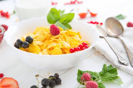 oatmeal with nuts and dried fruits on old white painted wooden table. Perfect breakfast Healthy tasty breakfast cornflakes with strawberries, raspberries, black currants and red currants.の写真素材