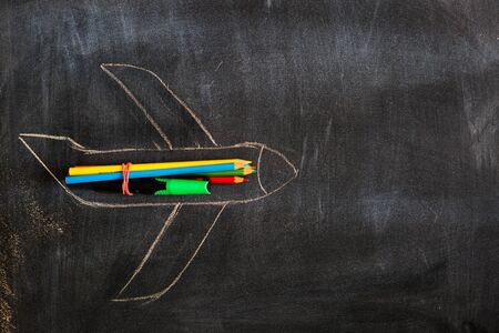 Back to school. Chalked drawing of an airplane on a school blackboard with school supplies and an empty place for your text or design.の写真素材