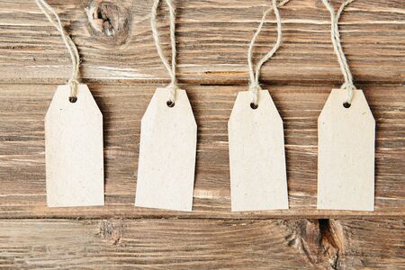 set of four tags hanging on rope on wooden background Four paper blank tags with rope on wooden background.の写真素材