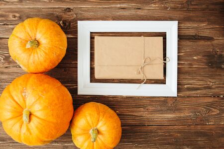 Pumpkins with white frame for picture and brown paper package tied up with strings inside over wooden background. Thanksgiving and Halloween concept. View from above.の写真素材