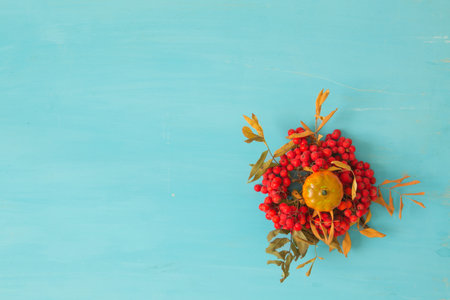 Autumn composition. Dried leaves, pumpkins, apple, flowers and rowan berries on blue background....