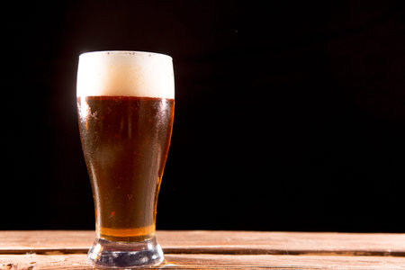 Cold tasty beer on a hot summer day. Glass of beer on wooden table on a black backgroundの写真素材