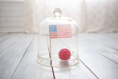 Ball in the form of a model of coronavirus Covid-19 and the US flag under a glass cover. America's...