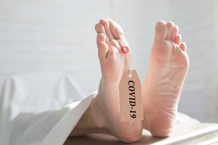 Legs of a corpse in a morgue on a table with a tag with the inscription COVID-19. Pandemic of the new coronavirus. Tragedy and deathの写真素材