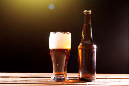 Cold tasty beer on hot summer day. Bottle and glass of beer on a wooden table against black background and copy spaceの写真素材