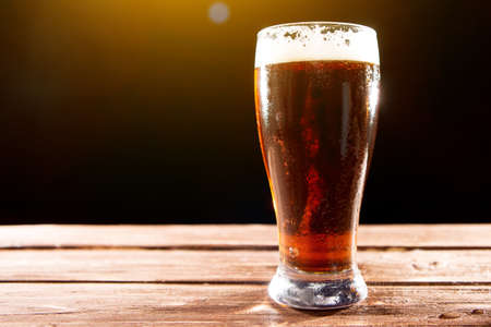 Cold tasty beer on hot summer day. Glass of beer on wooden table on black backgroundの写真素材