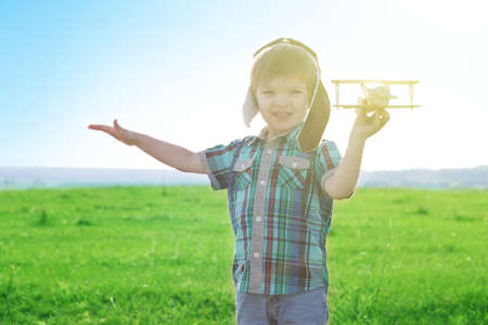 Start traveling from childhood even in imagination. Young Boy playing to be airplane pilot, funny guy with aviator cap and glasses, carries in his hand planeの写真素材