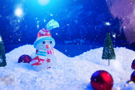 Snowman with Christmas balls on snow over fir-tree, night sky and moon. Shallow depth of field. Christmas background. Fairy tale. Macro. Artificial magic dreamy worldの写真素材