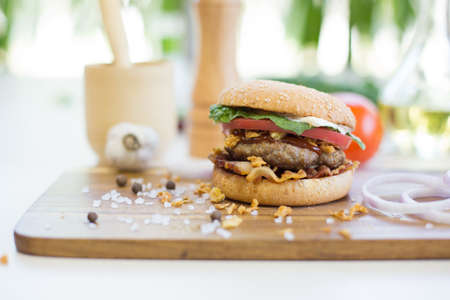 Appetizing hamburger on wooden cutting board. Pickles, onion, and cheddar cheese. Healthy and tasty food.の写真素材