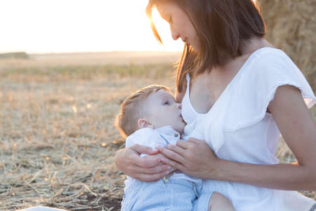 Beautiful happy mother breastfeeding her baby boy outdoor.の写真素材