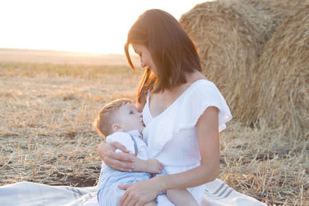 Beautiful happy mother breastfeeding her baby boy outdoor.の写真素材