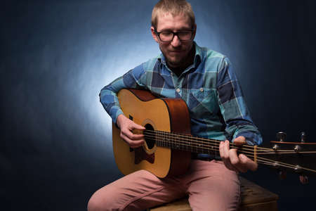 Handsome young musician playing the guitar on dark backgroundの写真素材