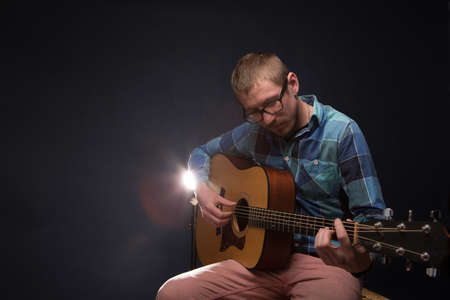 Handsome young musician playing the guitar on dark backgroundの写真素材