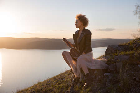 Woman with guitar ukulele in the mountains, amazing landscape, stunningly beautiful nature, mountains, sunset Hiking in the mountainsの写真素材