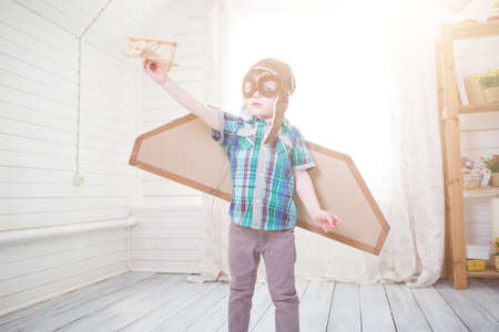 Children boy wearing pilot costume making ready to fly gesture standing on living room wooden floor at homeの写真素材